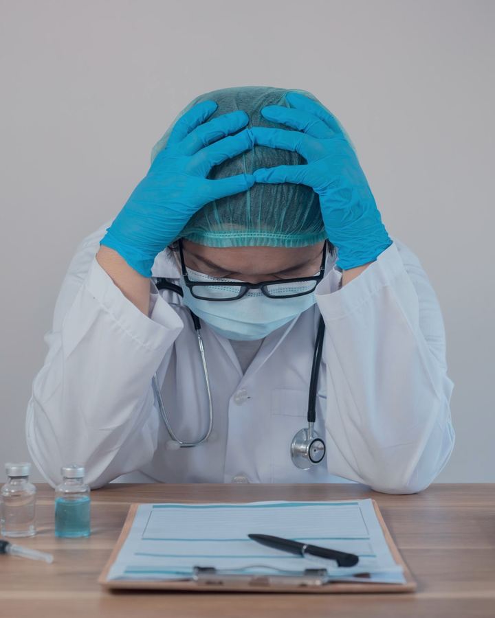 A clinician seated at a desk with their head in their hands